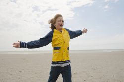 Junge steht mit ausgebreiteten Armen am Meer im Wind