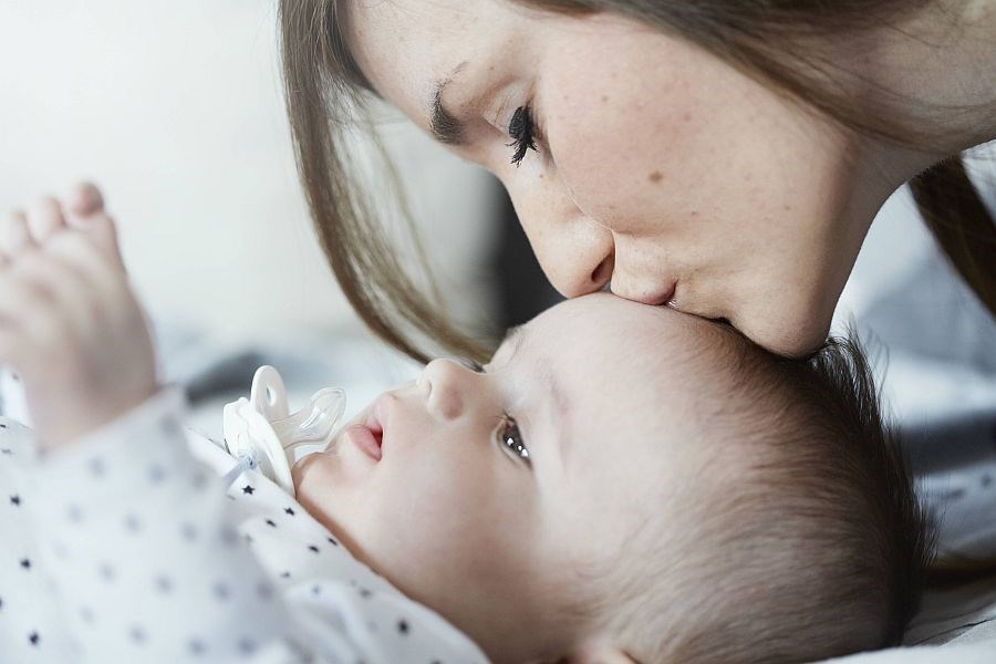 Mutter küsst Baby sanft auf die Stirn