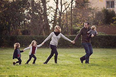 Vater, Mutter und drei Kinder halten sich an den Händen und laufen hintereinander über eine Wiese