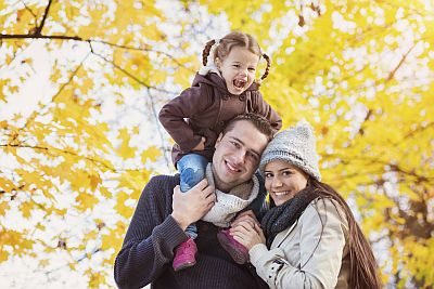 Vater, Mutter und Kind vor einem herbstlichen gefärbten Baum in der Sonne
