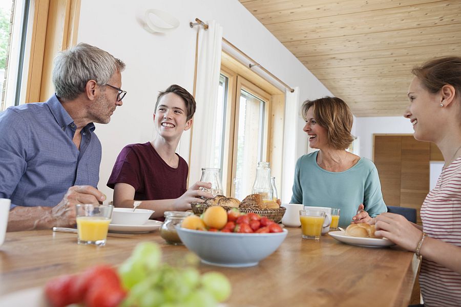Vater, Mutter und zwei jugendliche Kinder unterhalten sich fröhlich am Frühstückstisch
