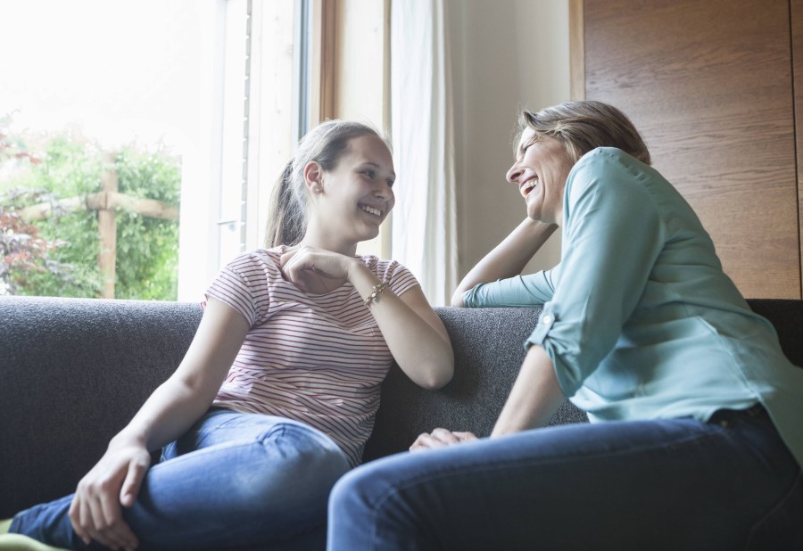 Mutter und Tochter unterhalten sich lachend auf dem Sofa