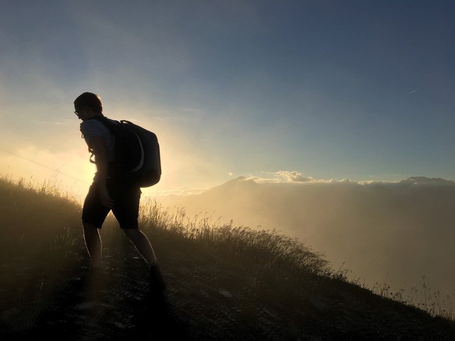 wandernder junger Mann auf Bergwiese im Sonnenaufgang