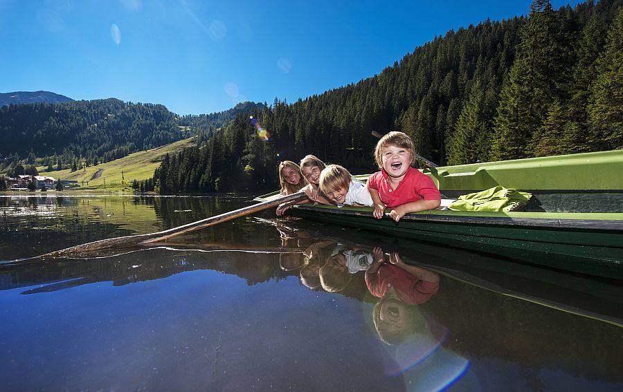 Kinder liegen entspannt in einem Ruderboot, das auf einem Bergsee treibt.
