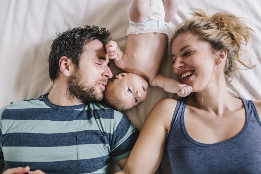 Vogelperspektive junge Eltern liegen lächelndmit Baby auf dem Bett