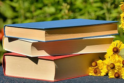 Bücher liegen auf einem Stapel, daneben Sonnenblumen.