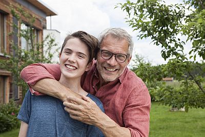 Vater legt jugendlichem Sohn die Arme um die Schultern, beide lachen