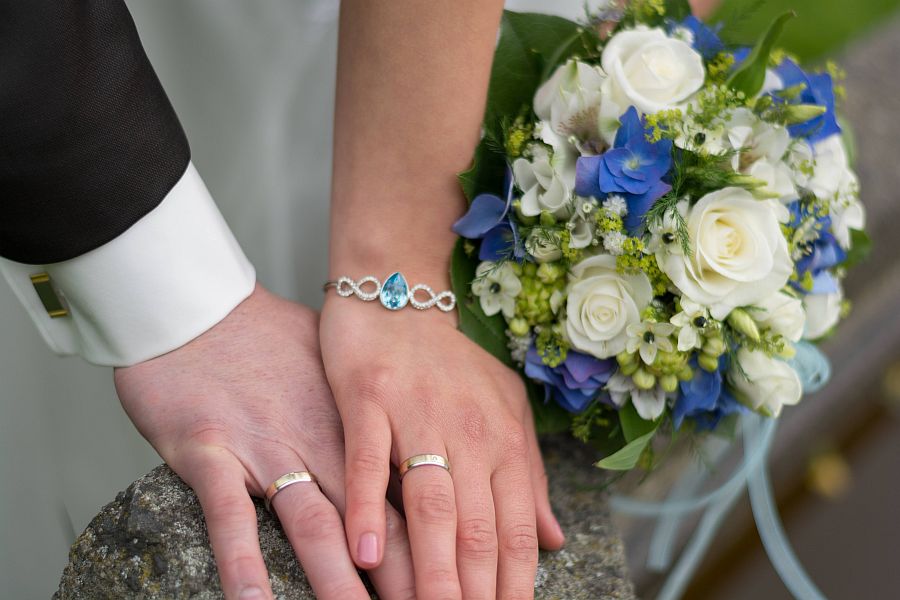 Hände von Brautpaar mit Ringen, daneben ein Blumenstrauß