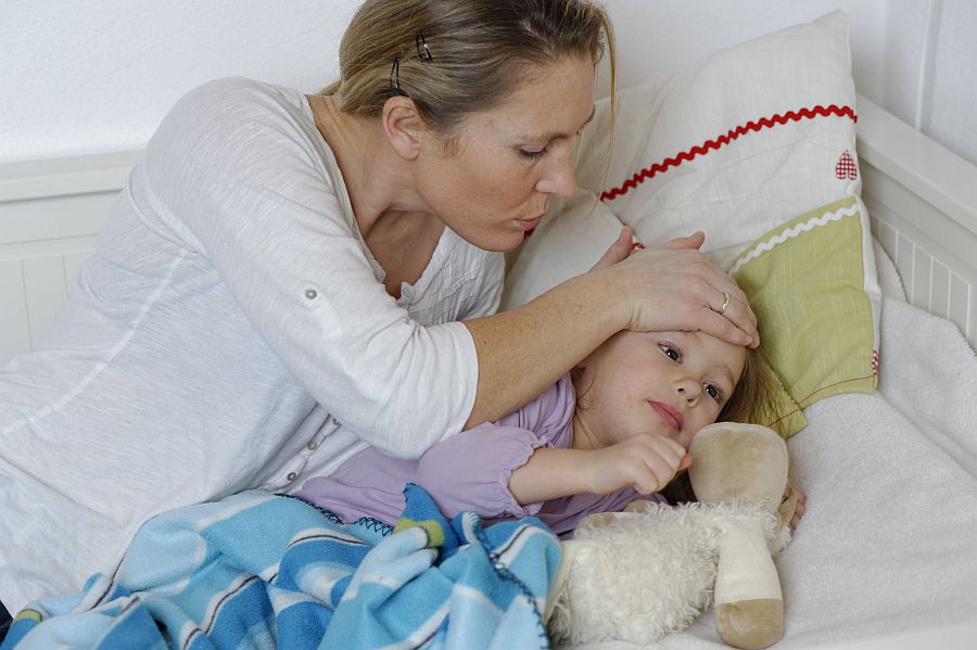 Mutter tröstet ein im Bett liegendes, krankes Mädchen.