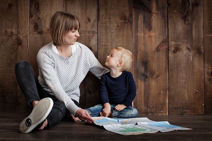 Mutter und etwa dreijähriger Sohn schauen zusammen auf einer Landkarte etwas an, Junge lacht, Mutter schaut skeptisch