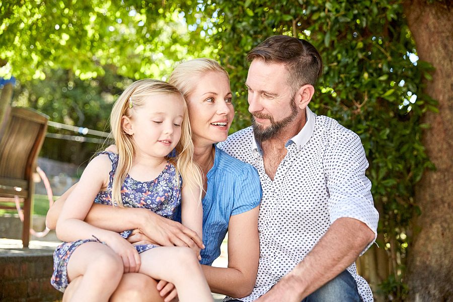 Vater, Mutter und Kind sitzen im Garten und sprechen miteinander.