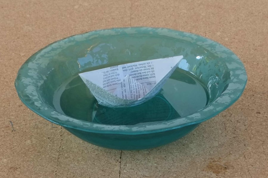kleines Papierschiff schwimmt in Wasserschale