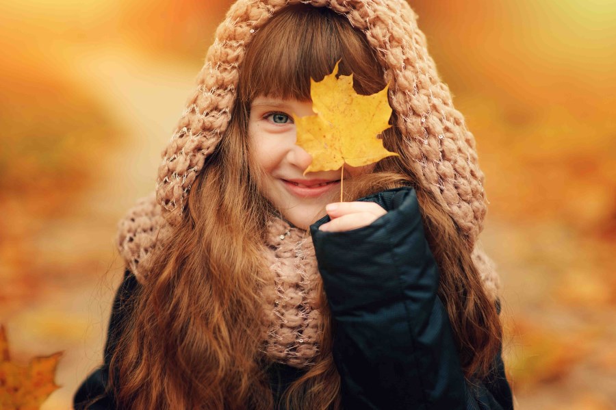 Mädchen mit Herbstblatt vor Gesicht